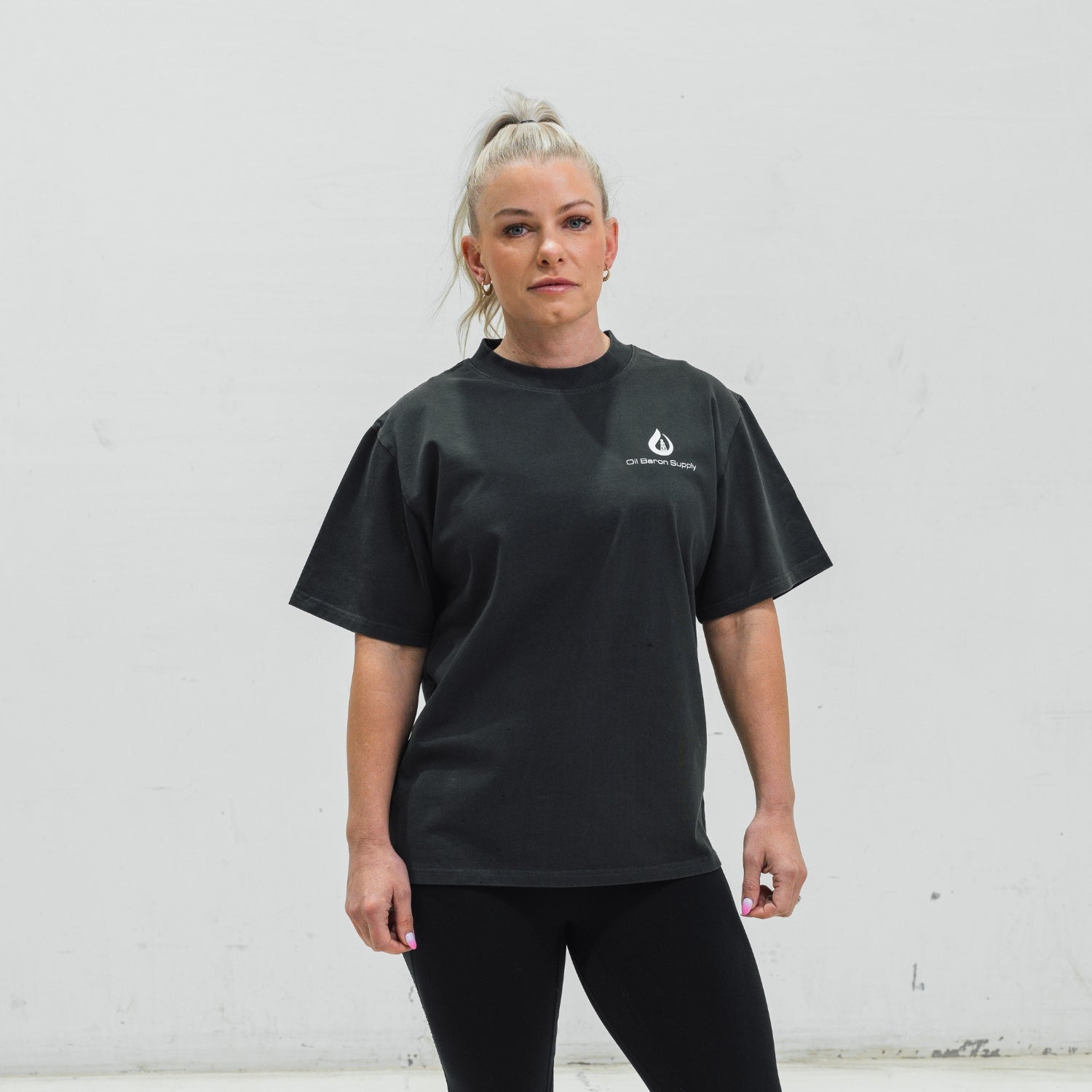 Woman wearing a black t-shirt with an oil baron supply logo against a white wall