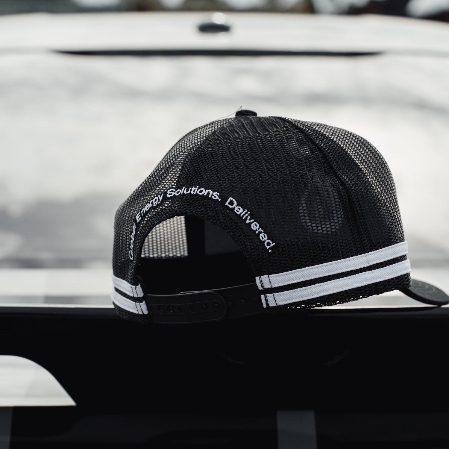 Black mesh cap with white text and stripes on a vehicle roof.