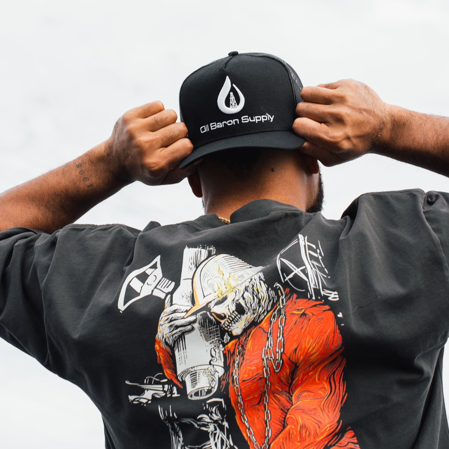 Person wearing a black cap with 'Oil Baron Supply' logo and a black shirt with a graphic design.