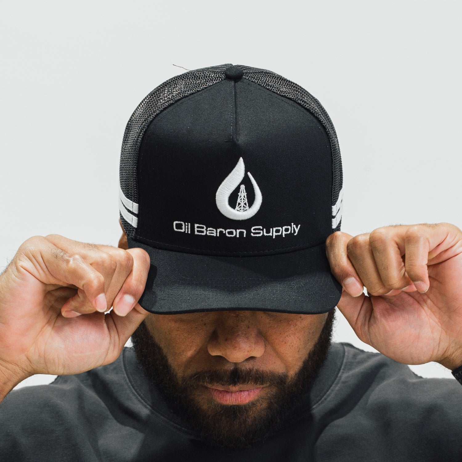 Person wearing a black cap with 'Oil Baron Supply' logo on a light gray background