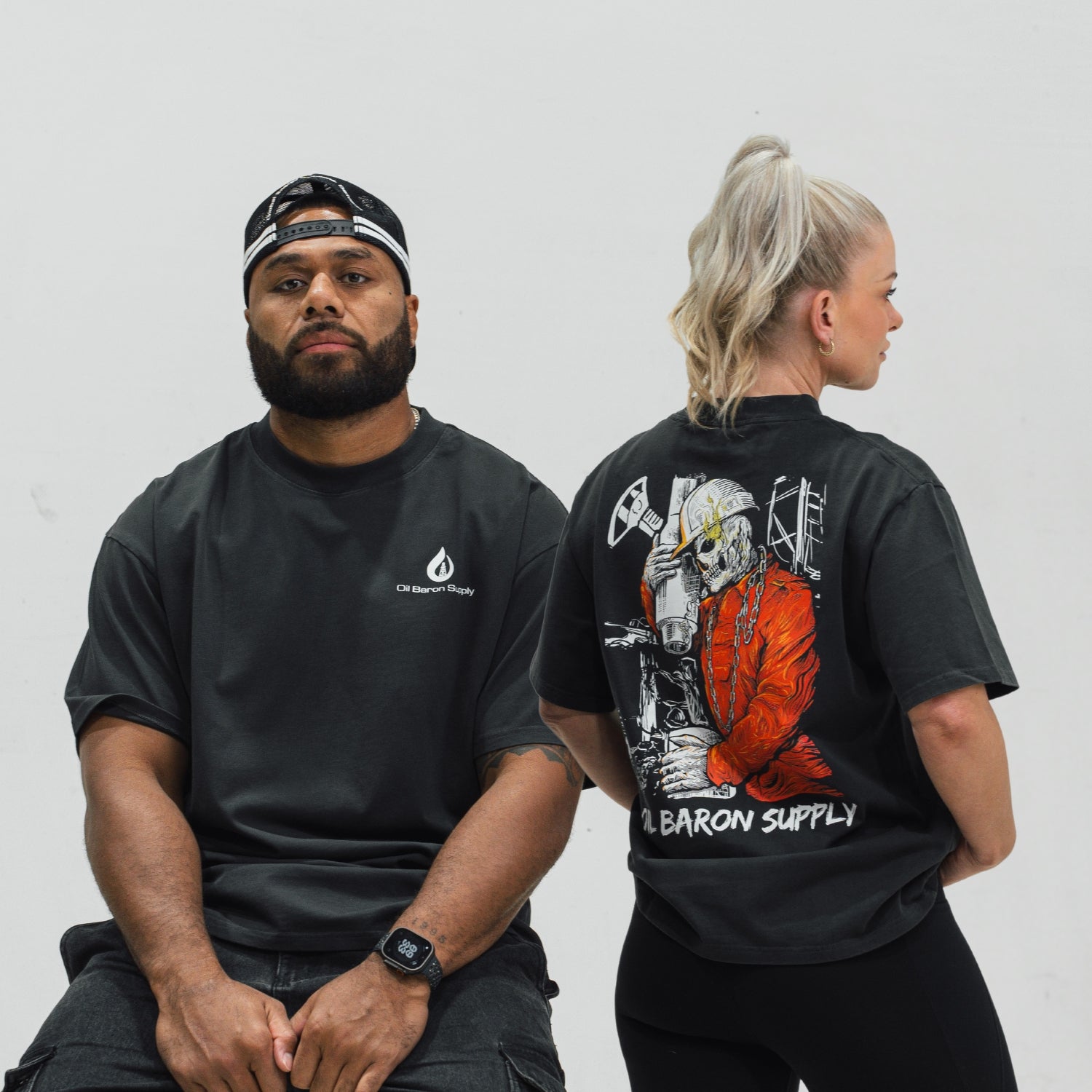 Two people wearing black t-shirts, one with an oil baron supply logo on the front and the other with a Roughneck design on the back.
