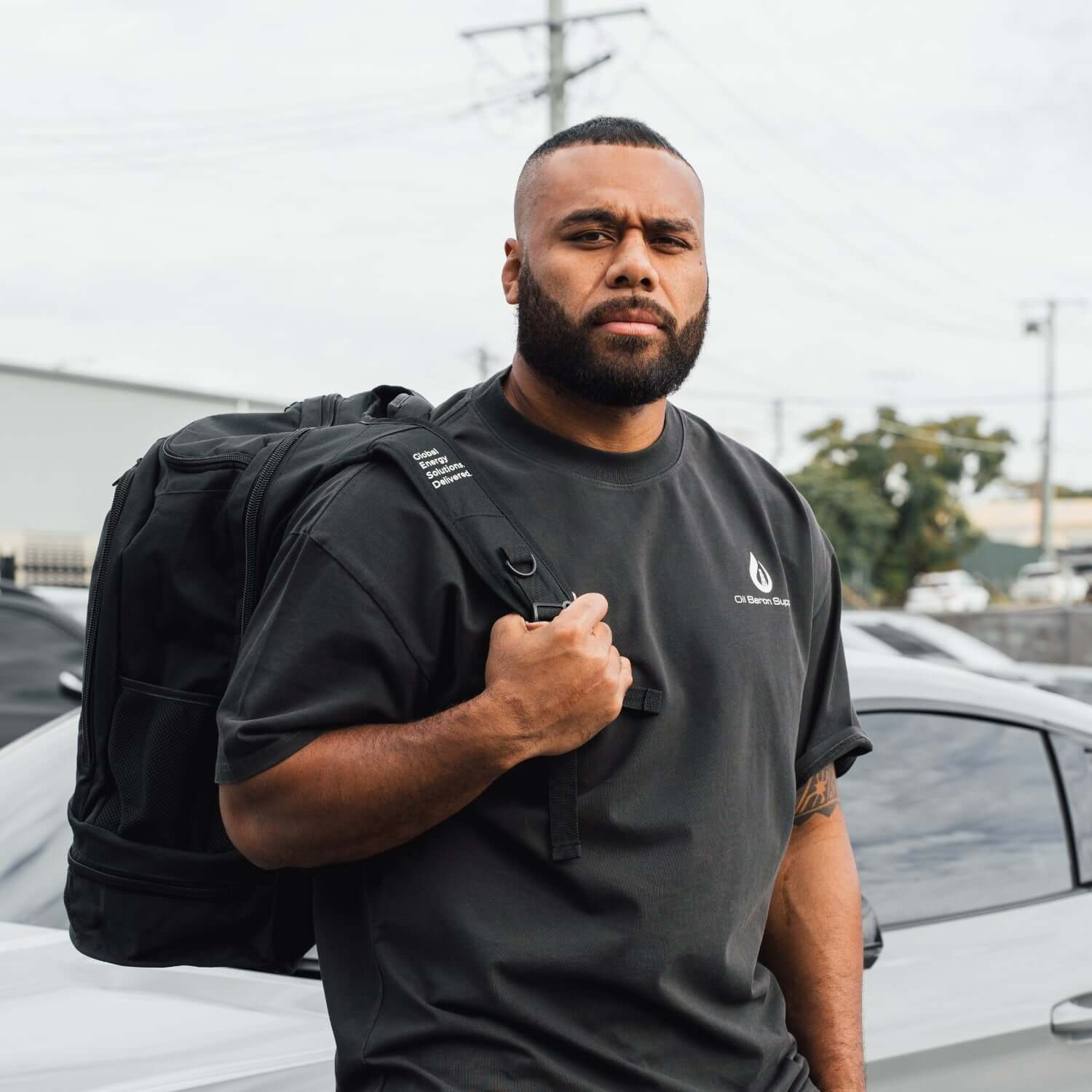 Man wearing a black t-shirt and carrying a black backpack outdoors.