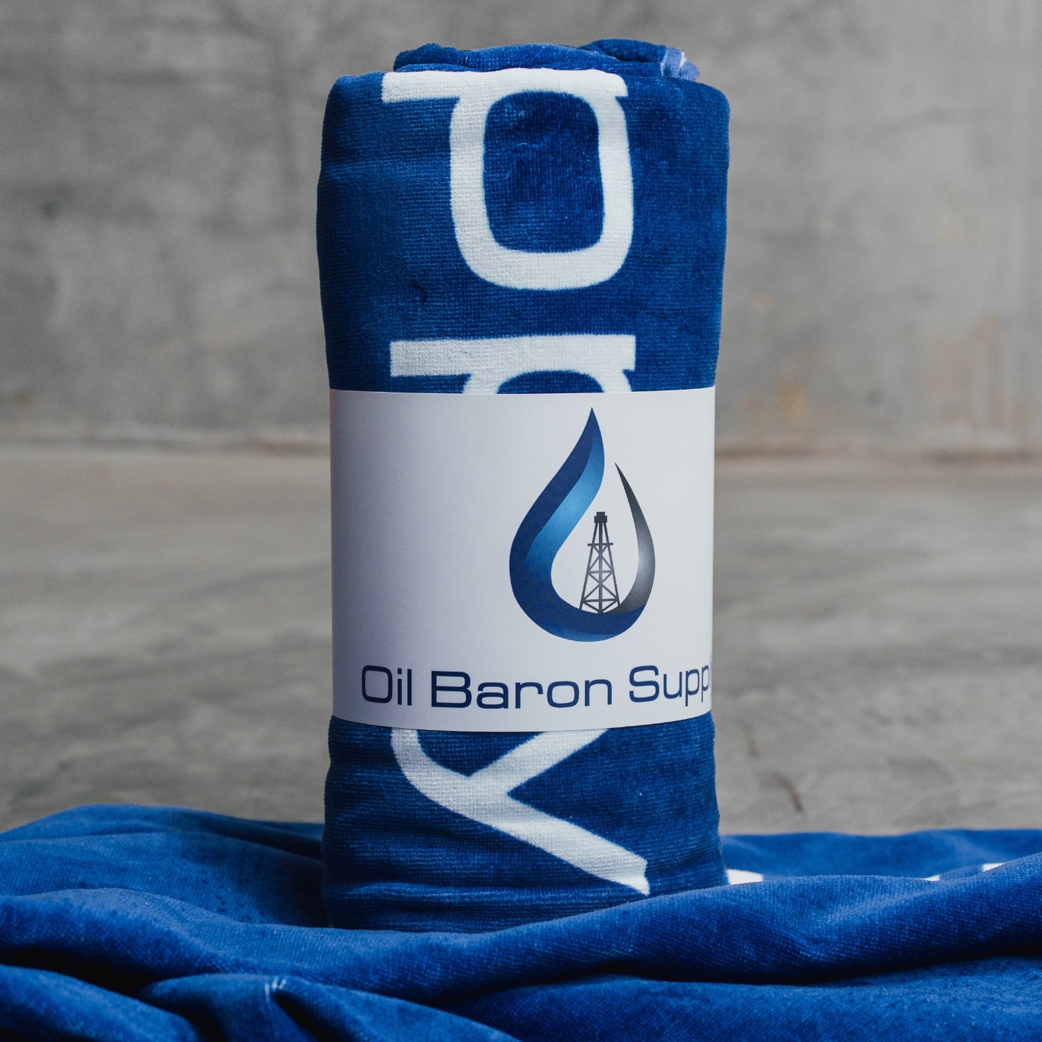 Blue and white towel with 'Oil Baron Supply' logo on a gray surface
