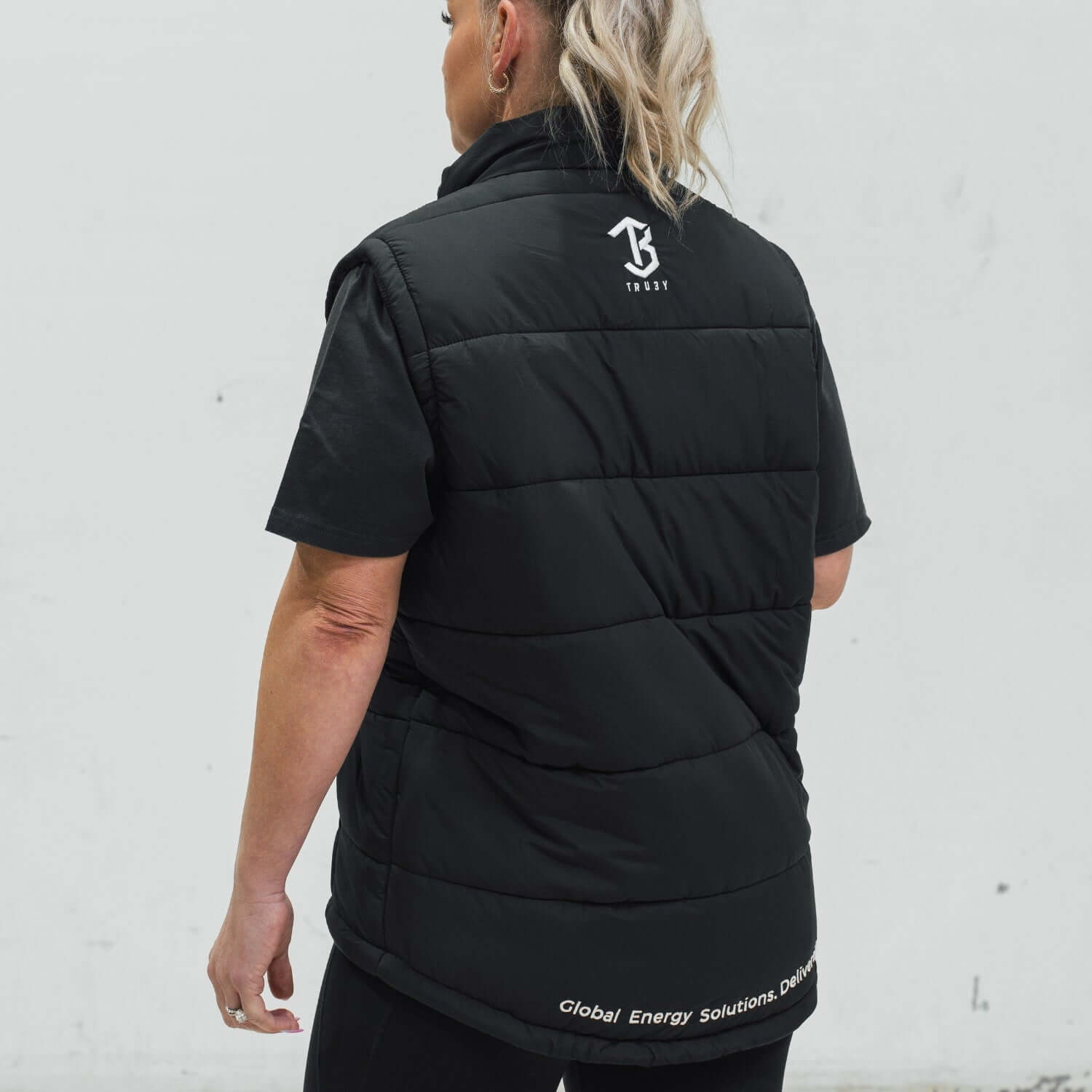 Person wearing a black puffer vest with a logo on the back against a white background