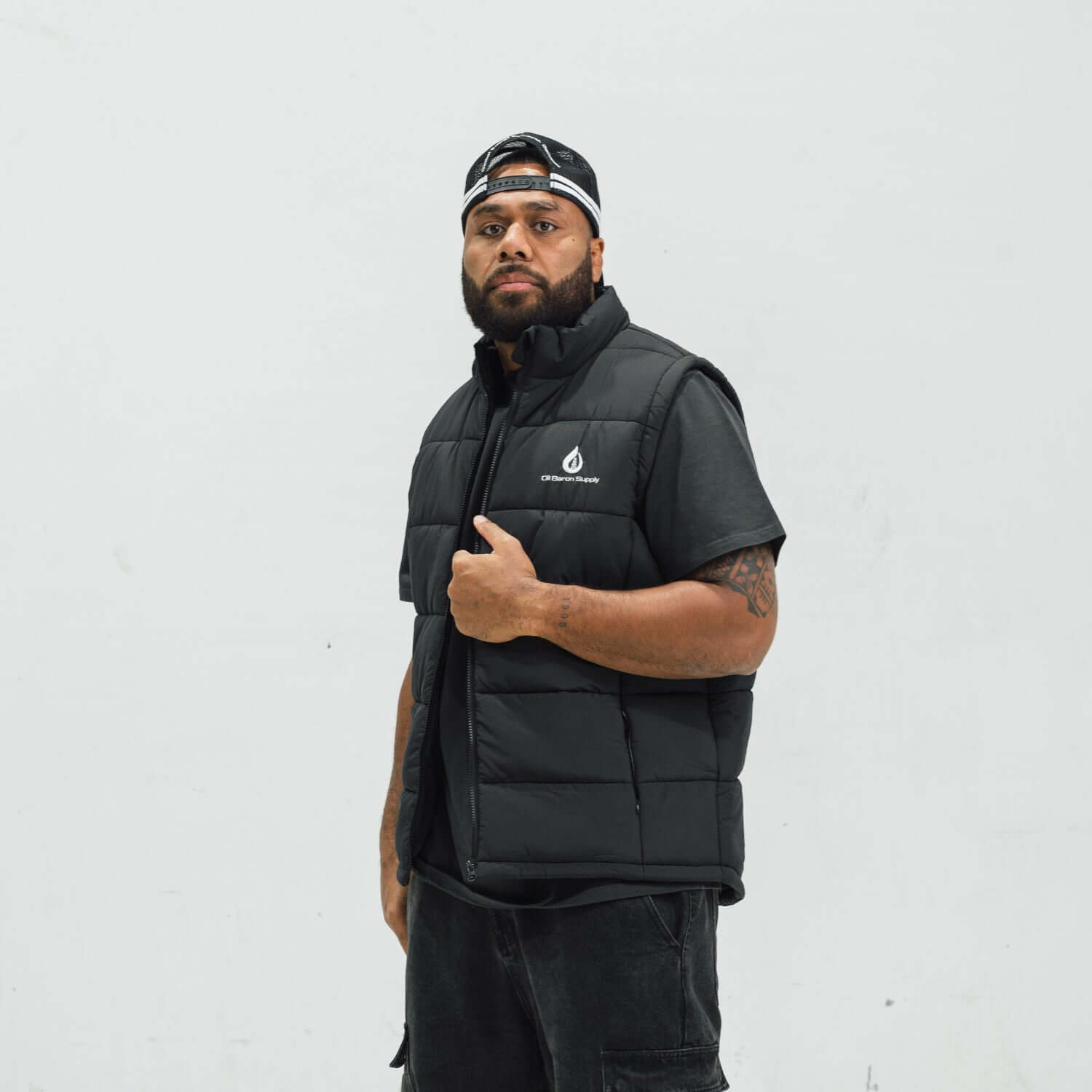 Man wearing a black puffer vest with a logo on a white background