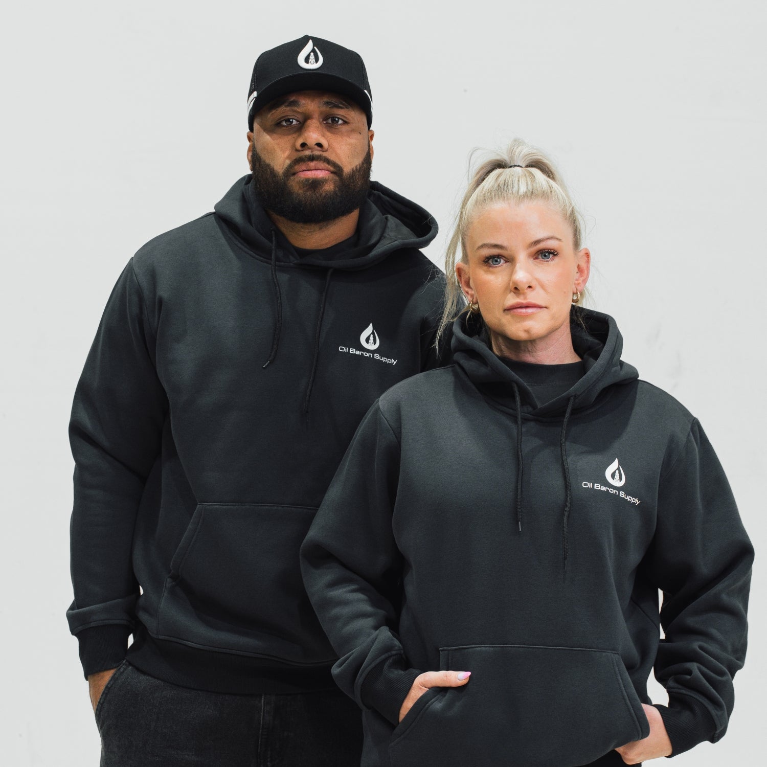 Two people wearing black hoodies with an oil baron supply logo on a plain background