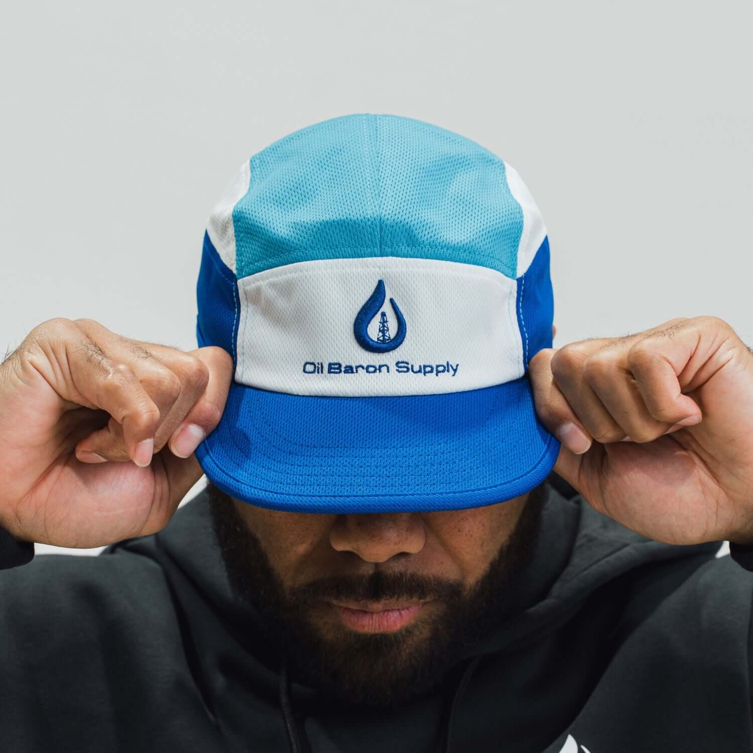 Person wearing a blue and white cap with 'Oil Baron Supply' logo on a gray background