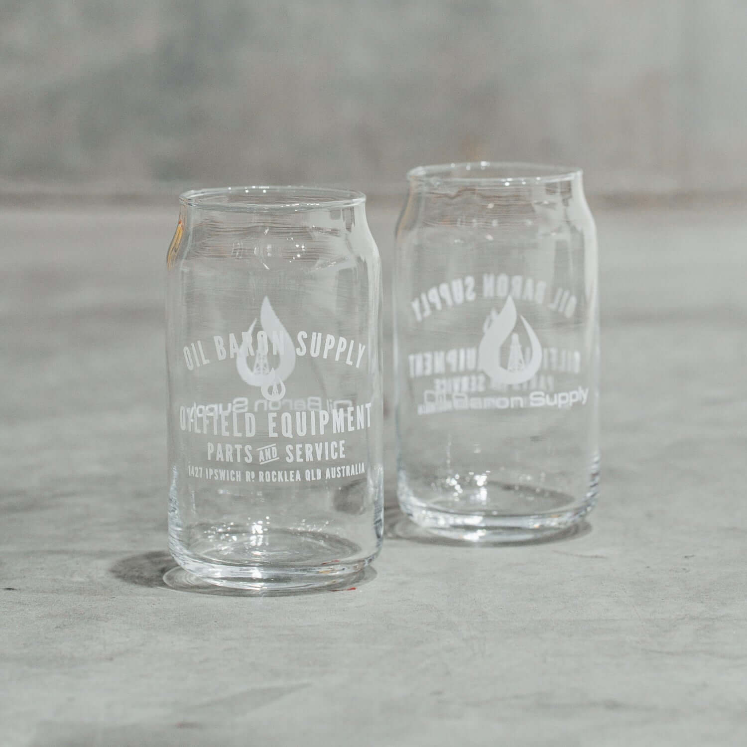 Two clear glass can-shaped tumblers with engraved text on a gray surface