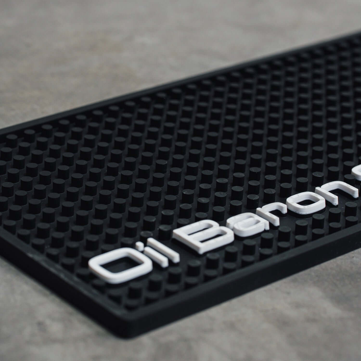 Black rubber mat with 'Oil Baron' branding on a gray surface