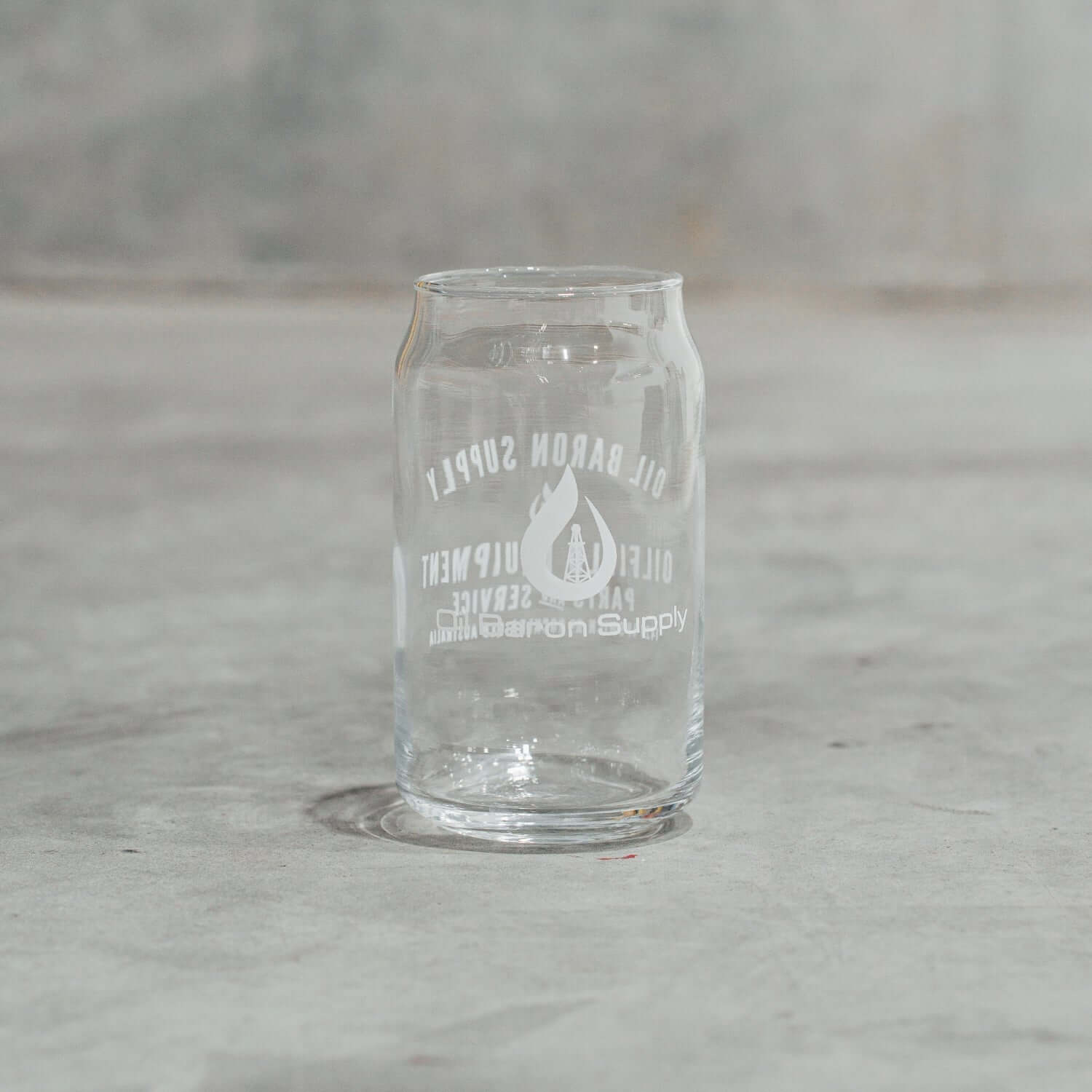 Clear glass can-shaped tumbler with engraved text on a gray surface