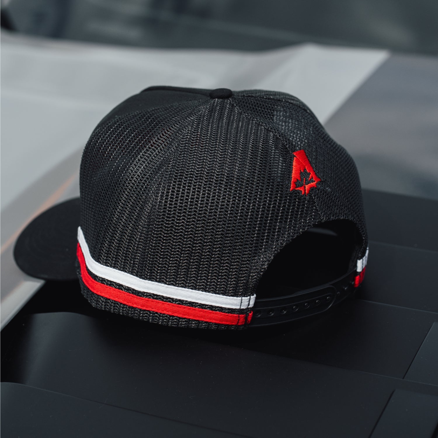 Black mesh cap with red and white accents on a car